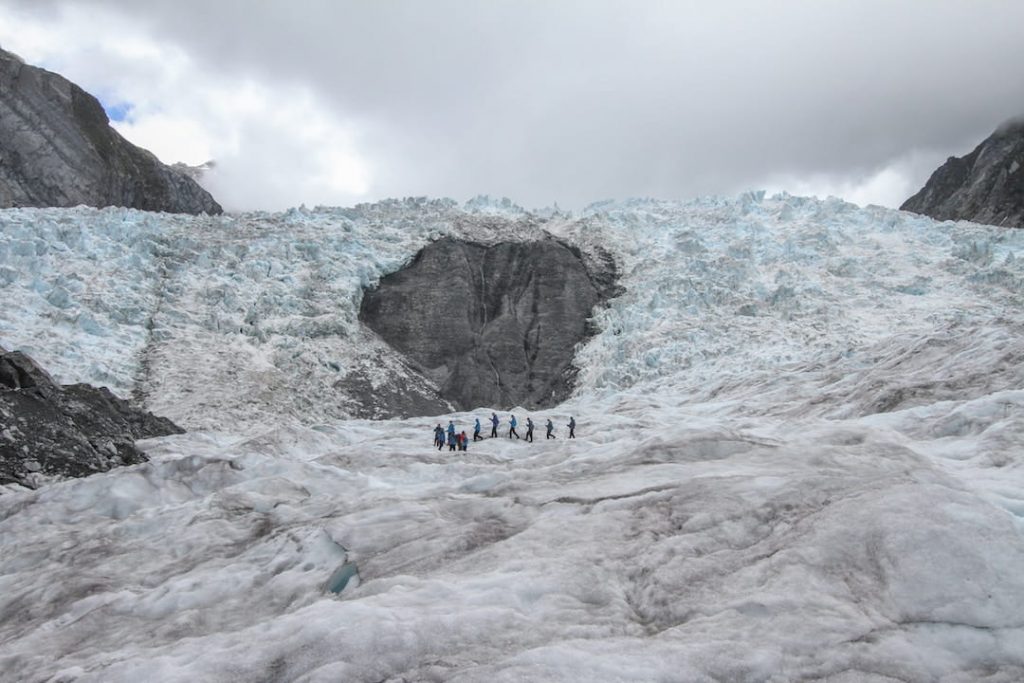 a group of people in winter coats hike along the Franz Josef Glacier in New Zealand